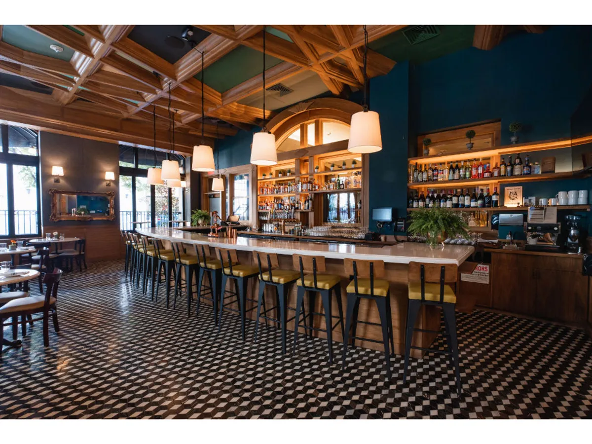 The vibrant bar area displays a contemporary counter with hanging lights and an eye-catching bottle display, creating a lively atmosphere ideal for socializing or enjoying a signature cocktail. The stylish floor tiles and seating add to the overall ambiance.