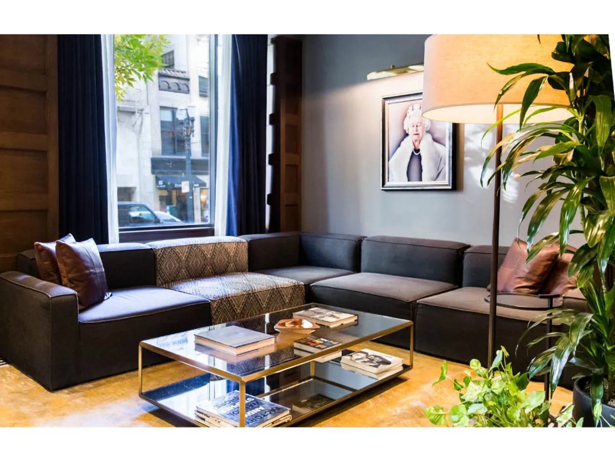 A stylish corner of a guestroom with a modern sectional sofa, glass coffee table, framed artwork, and large windows flooding the space with natural light. The area exudes a sense of sophistication and comfort, perfect for lounging or informal work.