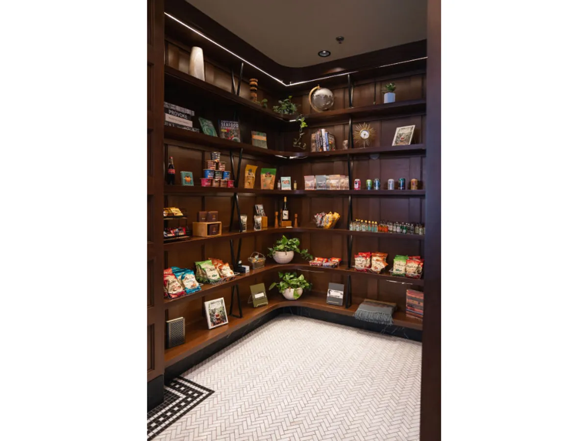 A cozy lounge or shop space featuring wooden shelves lined with local snacks, decorative items, and potted plants. The area has a casual, friendly feel, and the visible snacks and greenery evoke the idea of picking up treats—possibly even pet-friendly ones—after walking through the neighborhood.