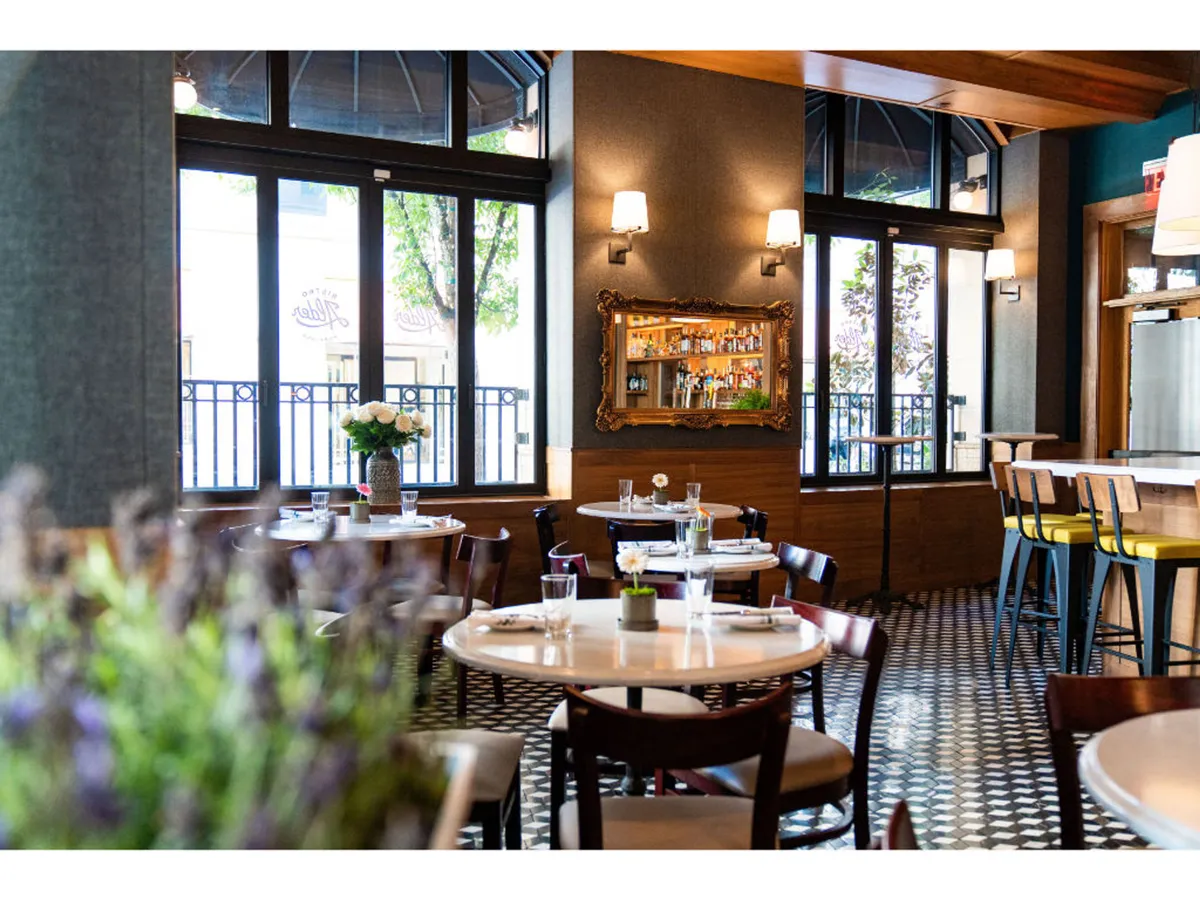 A cheerful dining area with tables adorned with fresh flowers, a mirrored bar, and expansive windows inviting daylight inside. The relaxed, sociable environment encourages friends to gather before exploring the city’s culinary and cultural highlights.
