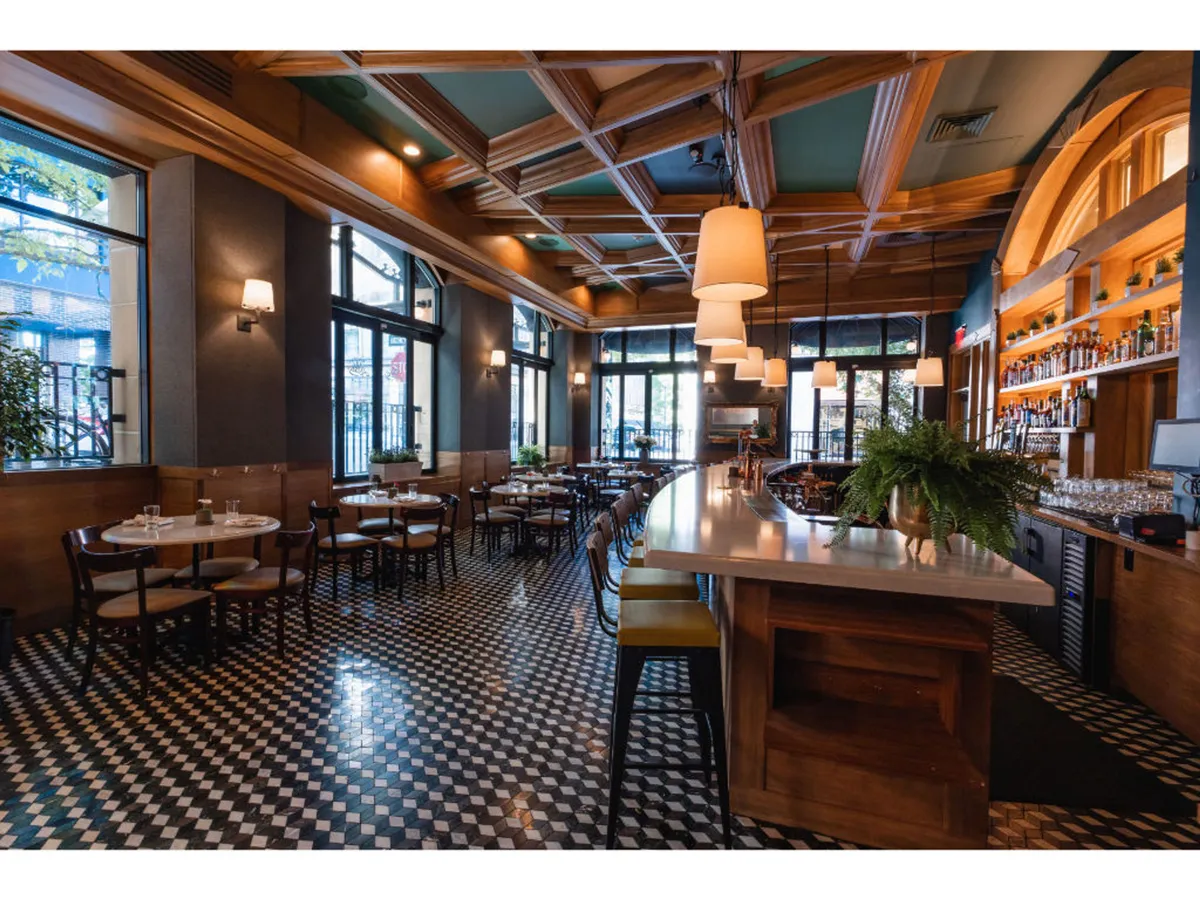 A spacious central bar area with a decorative ceiling, bathed in natural light from large windows. The room features dining tables ideal for mingling and savoring drinks, reflecting a sophisticated yet approachable atmosphere.